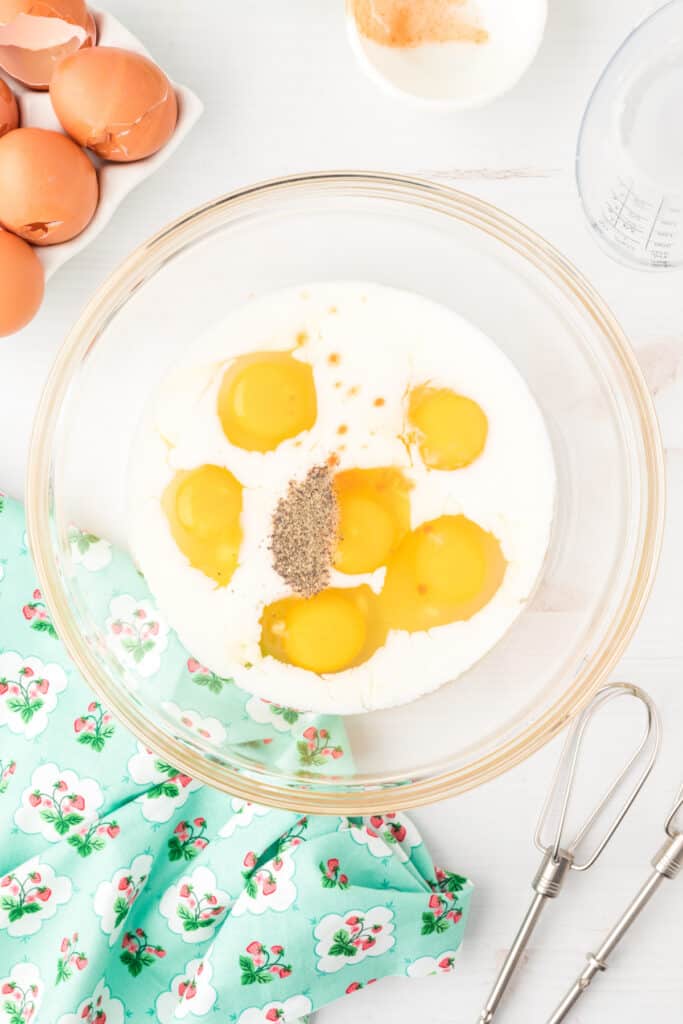 Eggs, milk, hot sauce, salt, and pepper in a glass bowl for Breakfast Egg Muffins