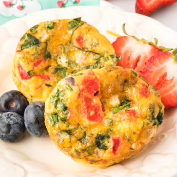 Breakfast Egg Muffins with spinach, roasted red peppers, and cheese served with strawberries and blueberries on a white plate
