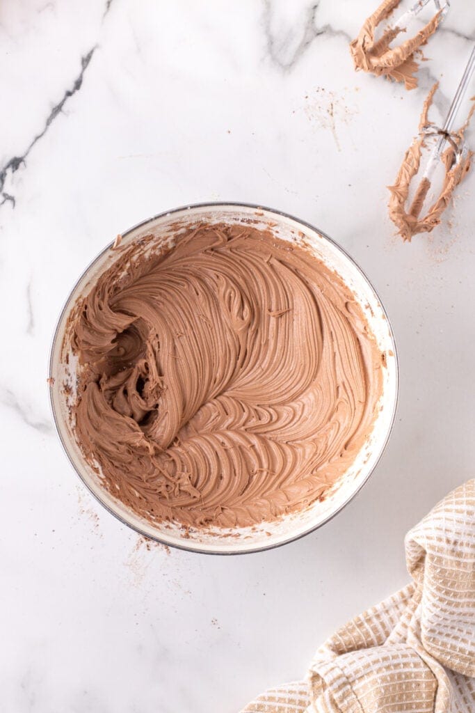 Bowl of whipped Nutella buttercream frosting showing creamy texture with beaters nearby.