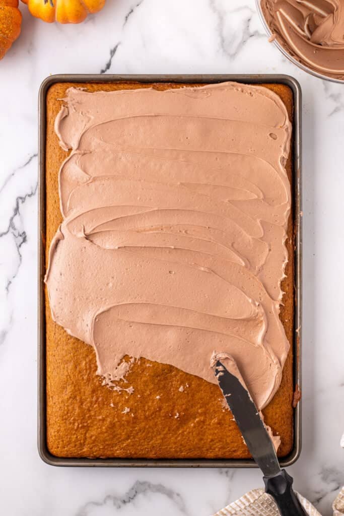 Pumpkin bars being frosted with Nutella buttercream using an offset spatula on a baking sheet.