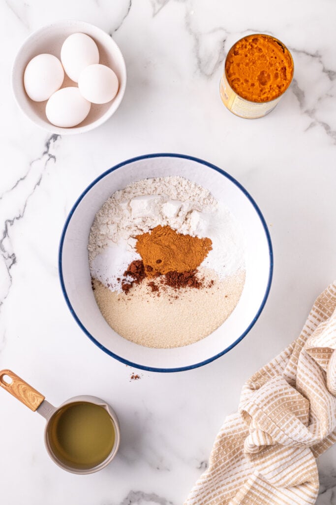 Mixing bowl filled with dry ingredients for pumpkin bars including flour, sugar, baking powder, cinnamon, and cloves.