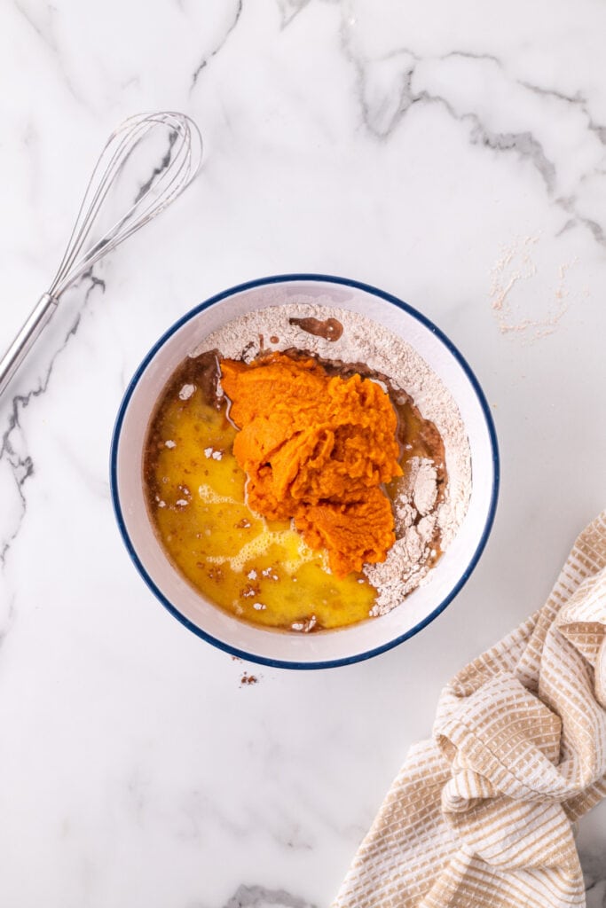 Pumpkin puree, eggs, and oil added to the bowl of dry ingredients before mixing for pumpkin bars.