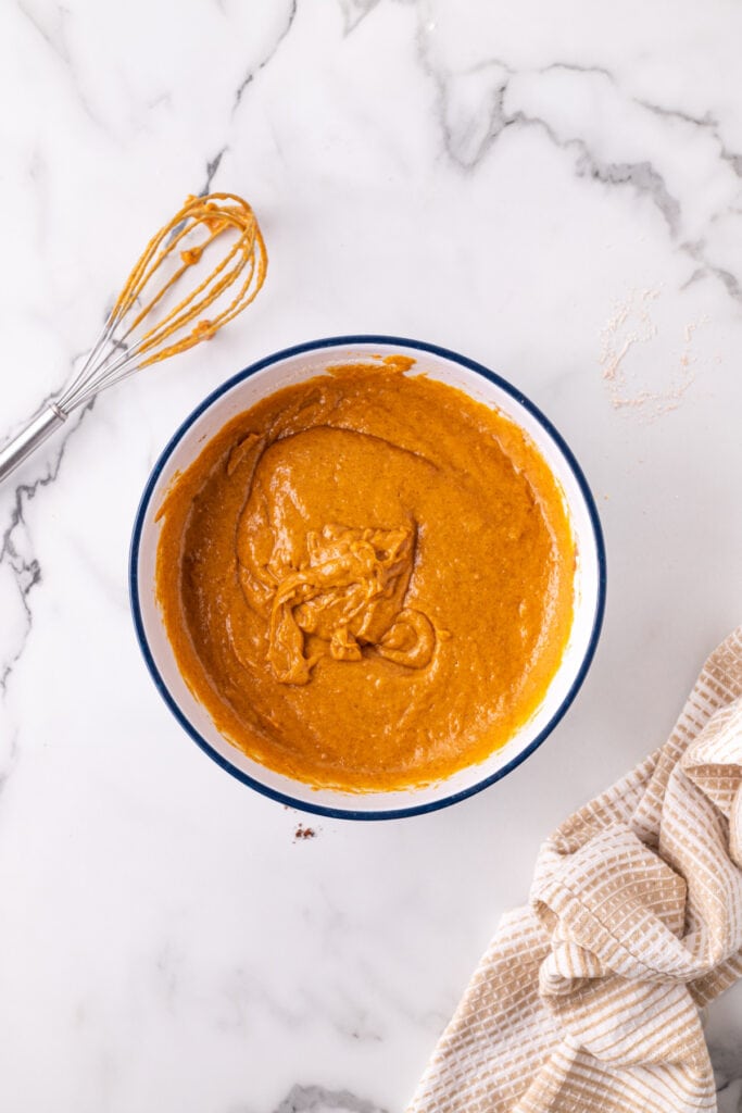 Pumpkin bar batter mixed until smooth in a large bowl with a whisk nearby on a marble countertop.