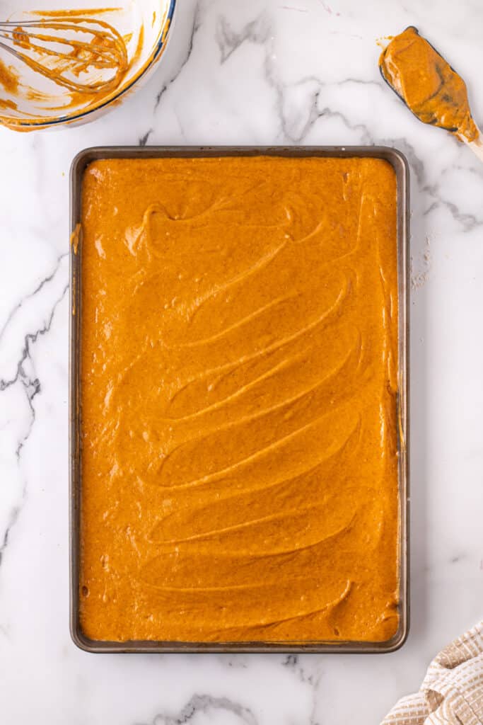 Pumpkin bar batter spread evenly into a parchment-lined baking sheet before baking.