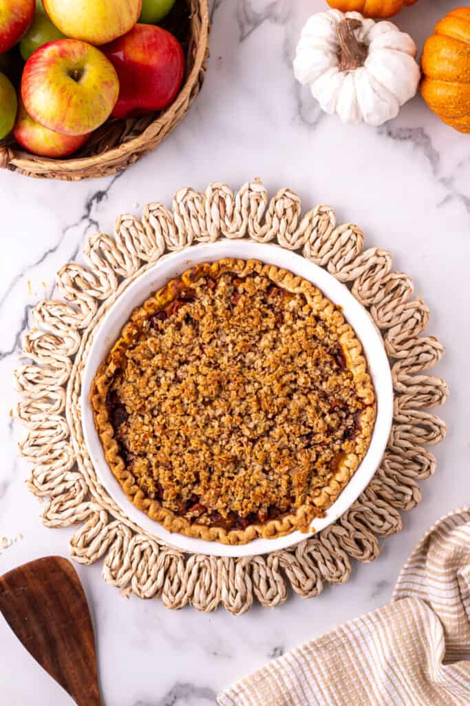 Fully baked Pumpkin Pie Apple Crisp resting in a white pie dish on a woven trivet.