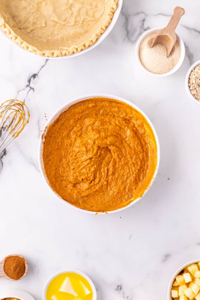 Mixed pumpkin filling in a bowl ready to be poured into the pie crust for Pumpkin Pie Apple Crisp.