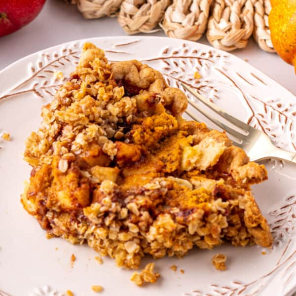 Slice of Pumpkin Pie Apple Crisp on a decorative plate with a fork, showing the crumb topping and pumpkin apple filling.
