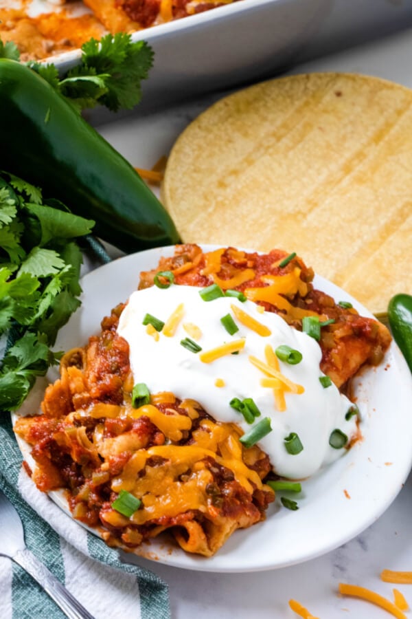 two ground beef enchiladas on plate with sour cream