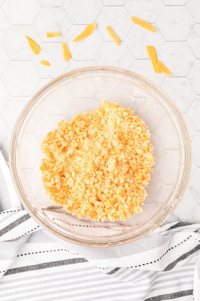 Crumbly dough mixture for homemade cheese bites in a clear glass bowl before rolling and baking