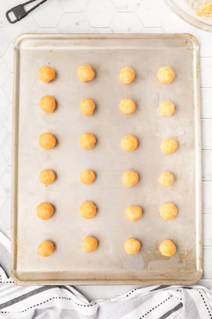 Unbaked cheese bites arranged on a baking sheet before baking