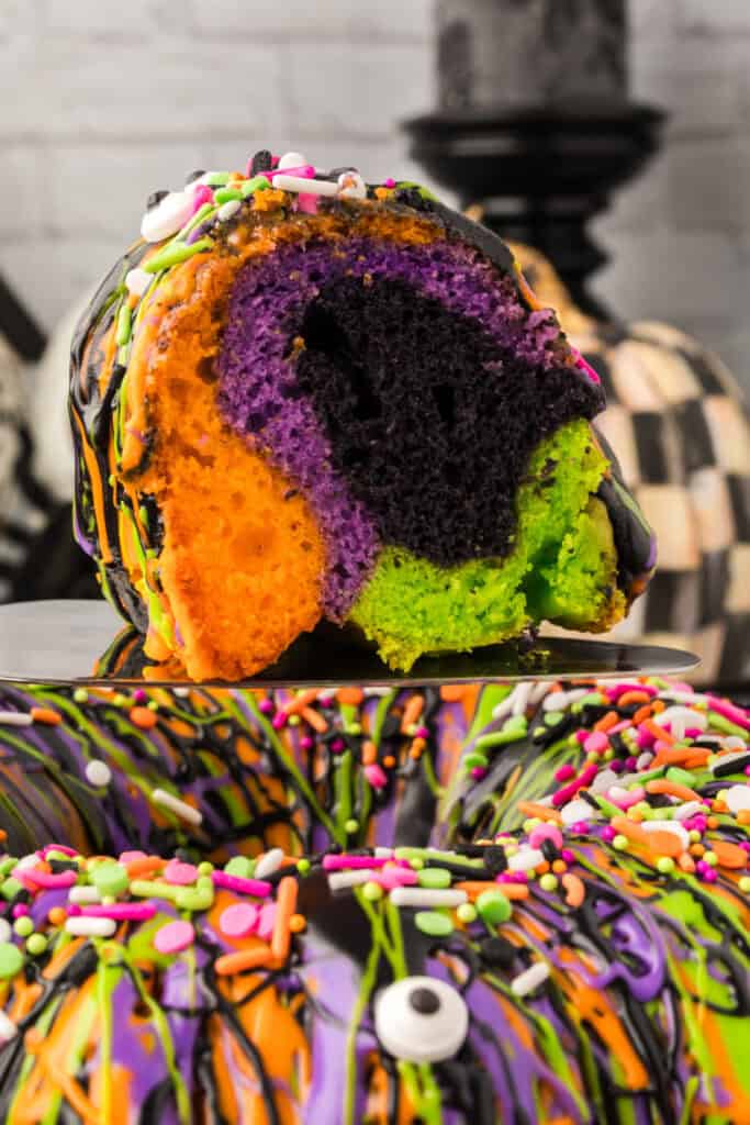 Close-up slice of Halloween Bundt Cake showing orange, purple, black, and green layers with festive sprinkles.