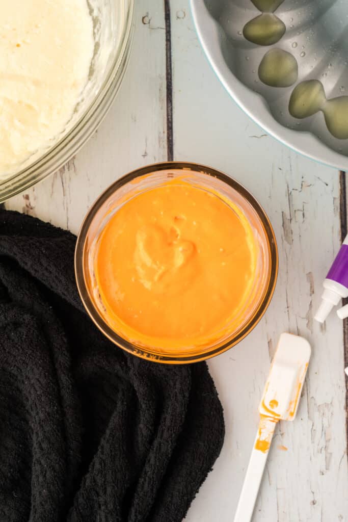 Bowl of orange cake batter with a white spatula resting beside it for Halloween Bundt Cake layers.