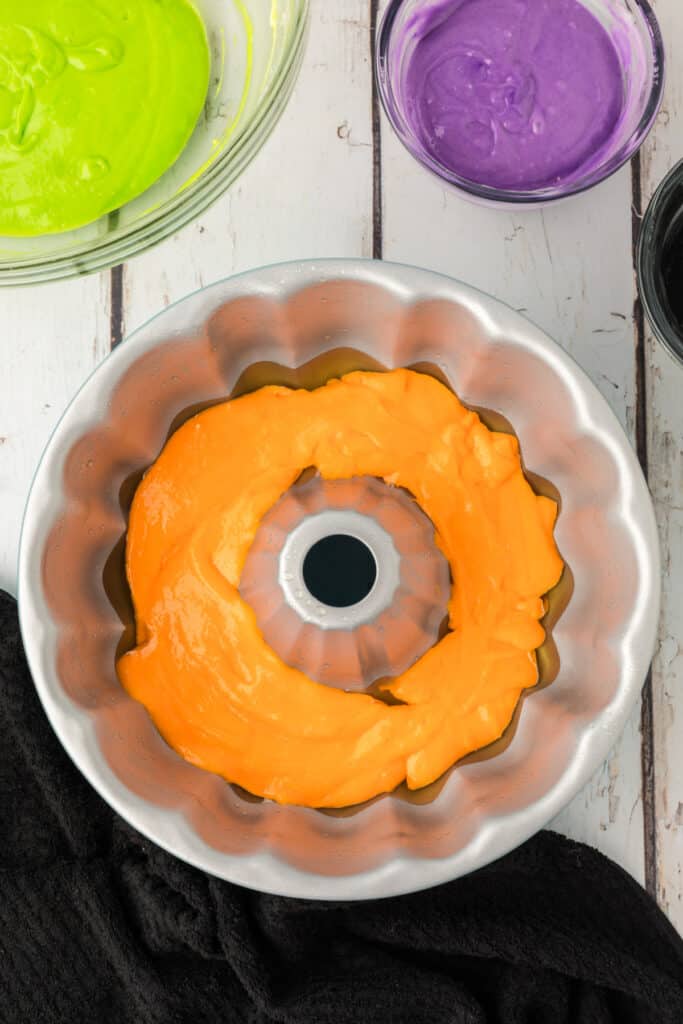 Orange cake batter spread evenly in the bottom of a greased bundt pan for Halloween Bundt Cake base layer.