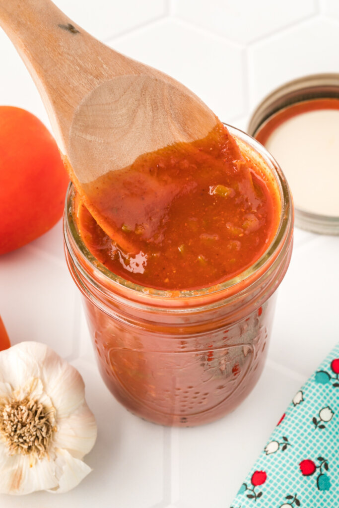 wooden spoon scooping homemade enchilada sauce out of a glass jar