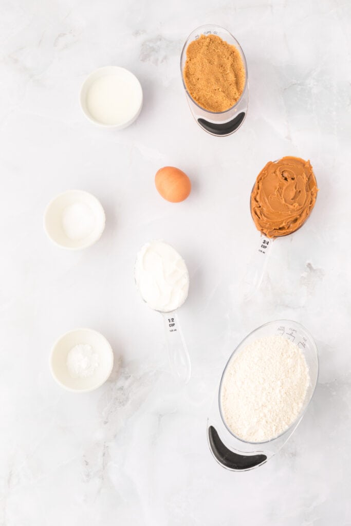 biscoff butter cookies ingredients including cookie butter, brown sugar, flour, egg, milk, and shortening on a white surface