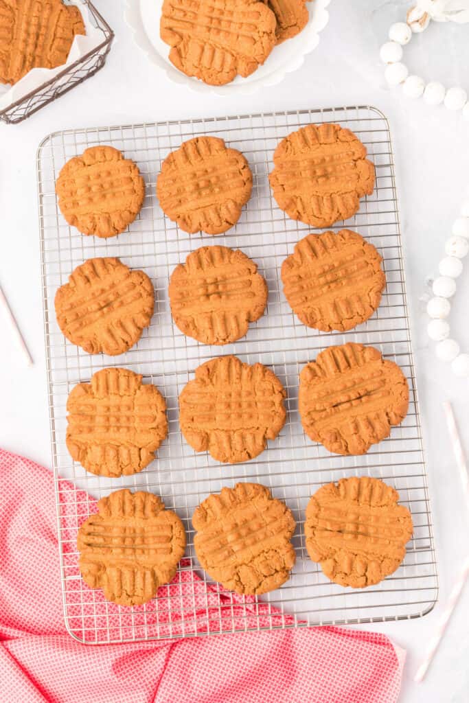 biscoff butter cookies cooling on a wire rack with a white plate and jar of lotus biscoff cookie butter in the background