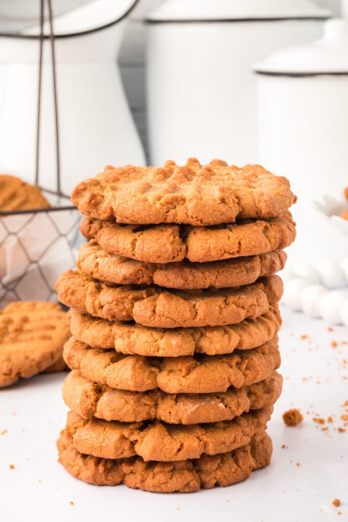 stack of biscoff butter cookies on white surface with a wire basket of cookies and blurred background decor