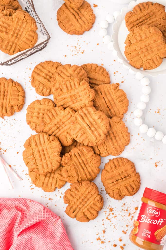 stack of biscoff butter cookies on white surface with jar of lotus biscoff cookie butter in the background