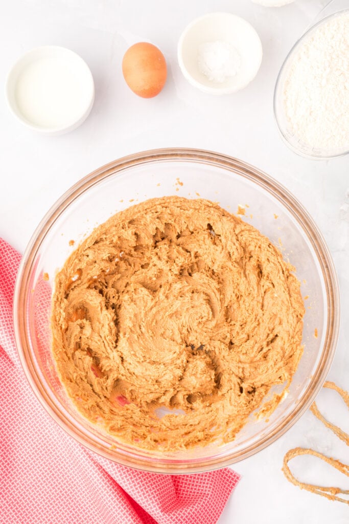 creamed mixture for Biscoff Butter Cookies in a glass mixing bowl with hand mixer beaters nearby