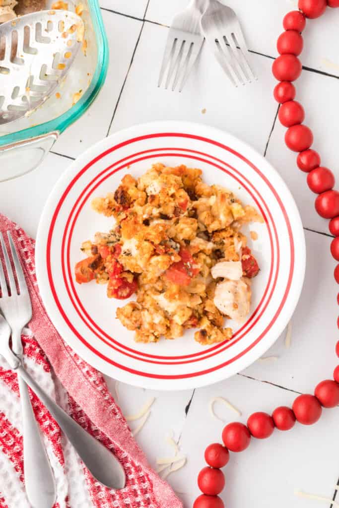 Overhead view of a plated serving of Chicken Bruschetta Bake with visible chicken, tomatoes, melted cheese, and golden stuffing topping on a white plate with red stripes.