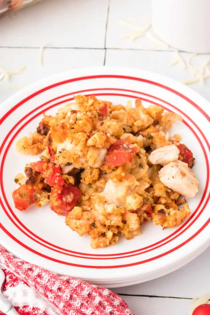 Chicken Bruschetta Bake served on a white plate with red stripes, showing tender chicken pieces, diced tomatoes, melted mozzarella cheese, and toasted stuffing topping.