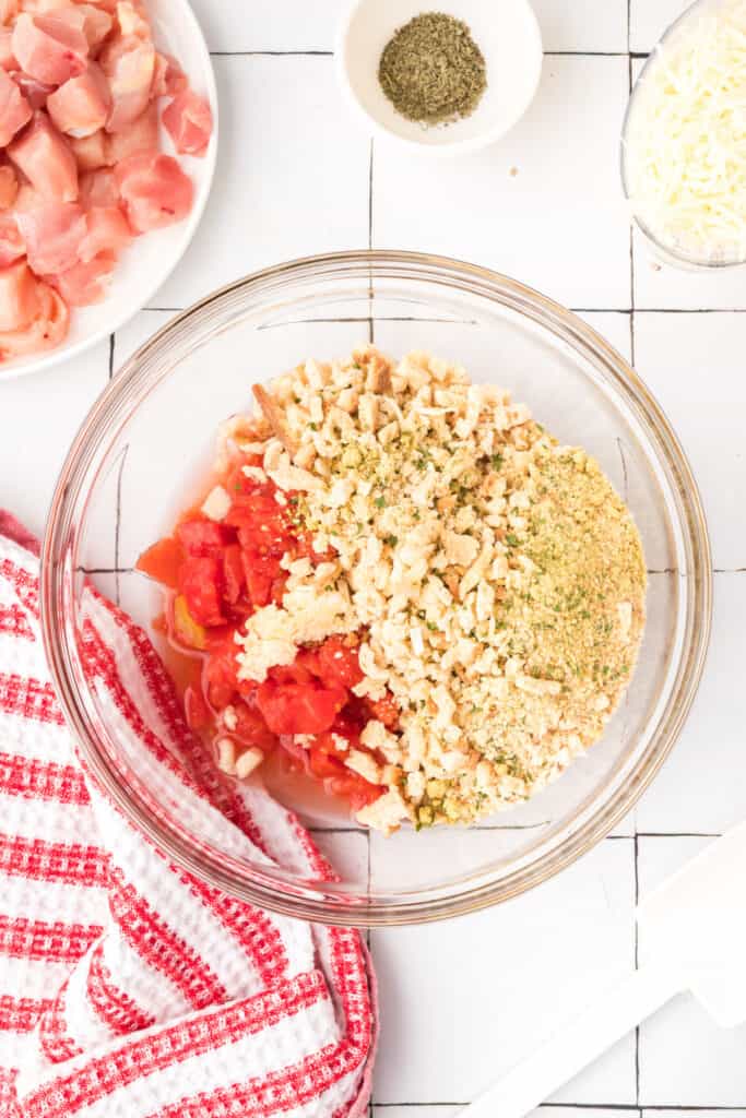 Diced tomatoes, stuffing mix, garlic, and seasonings in a glass mixing bowl for Chicken Bruschetta Bake before stirring.