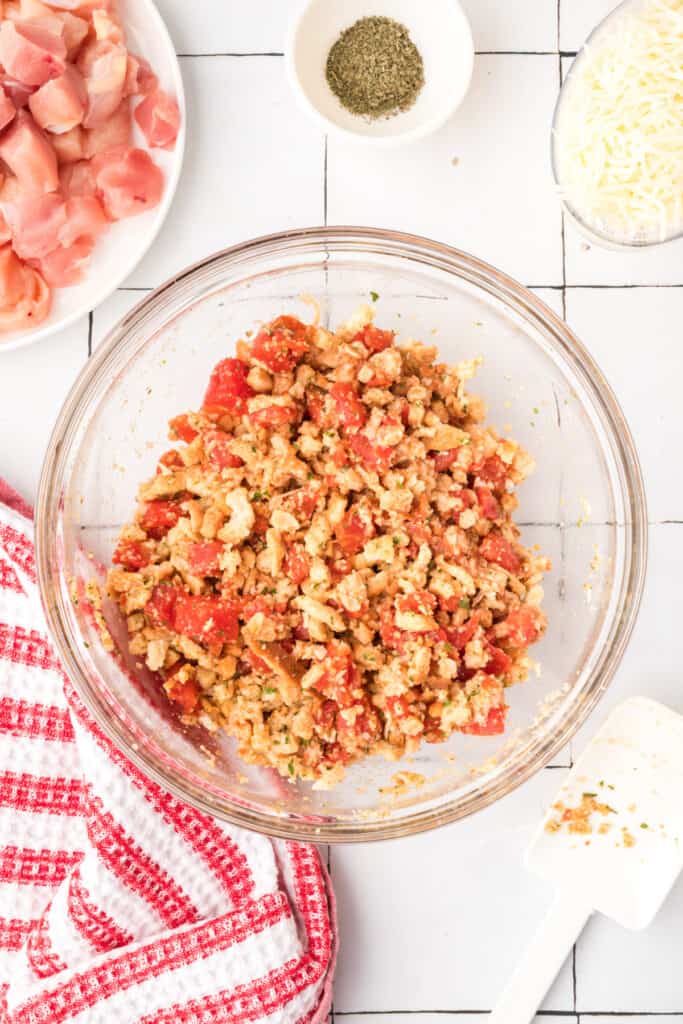 Stuffing mixture combined with diced tomatoes and seasonings in a glass bowl for Chicken Bruschetta Bake.