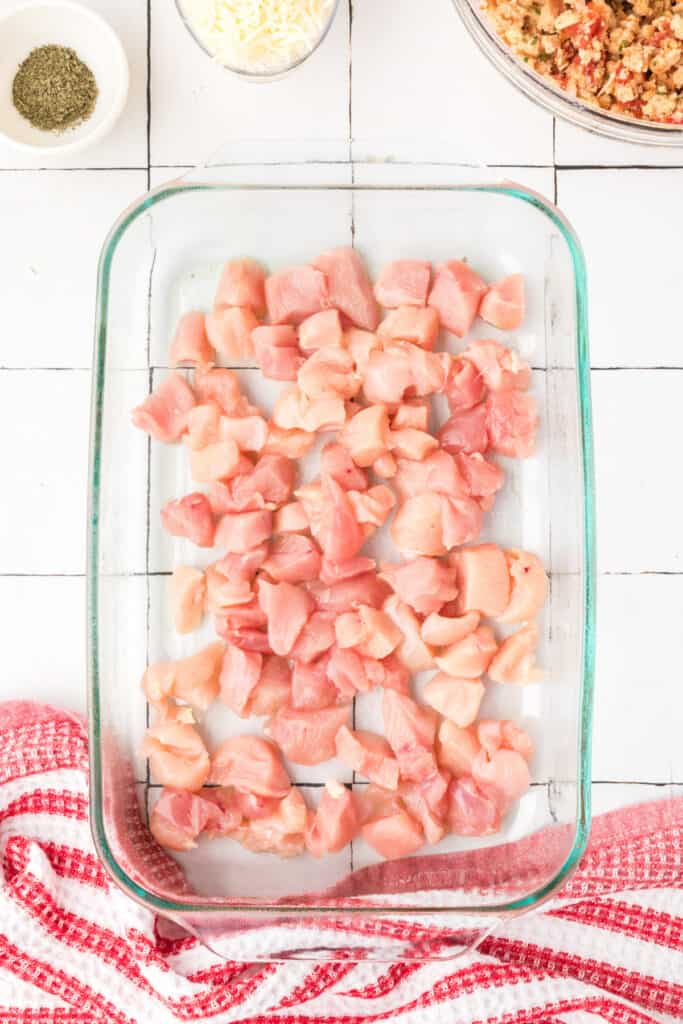 Bite-sized chicken breast pieces arranged in a greased glass baking dish for Chicken Bruschetta Bake.