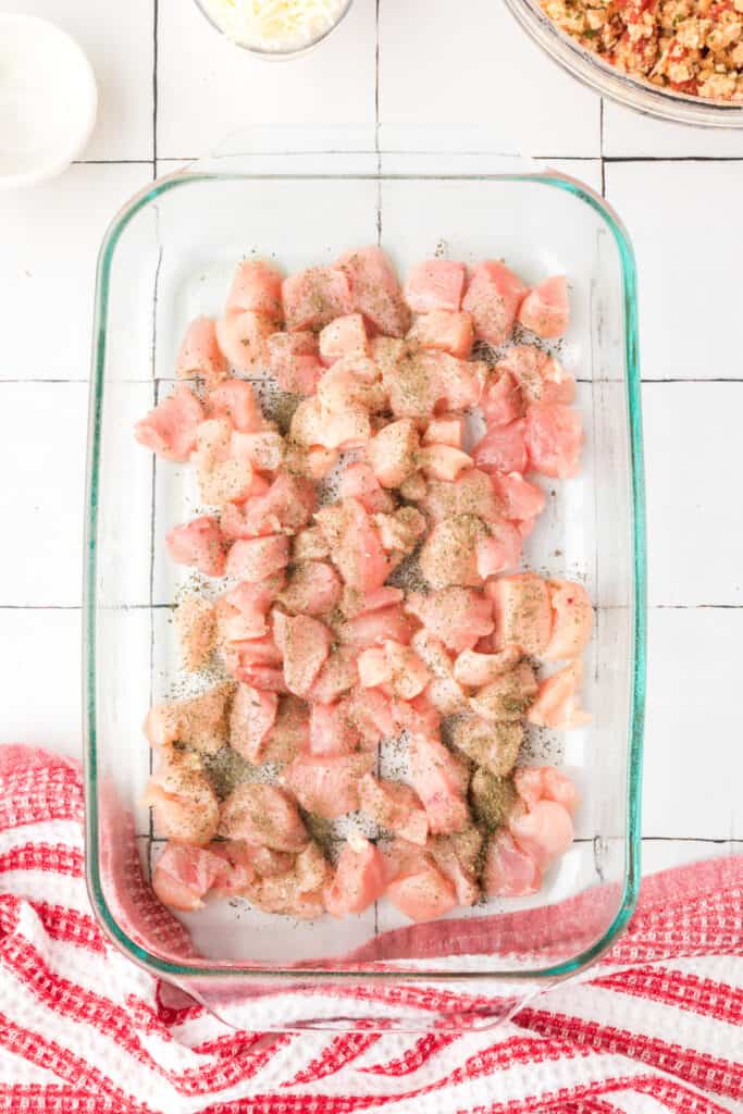 Chicken breast pieces in a baking dish sprinkled with dried basil for Chicken Bruschetta Bake.
