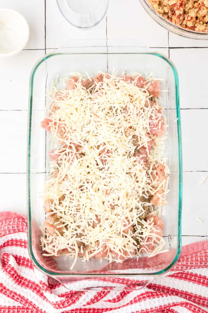 Chicken breast pieces topped with shredded mozzarella cheese in a baking dish for Chicken Bruschetta Bake.