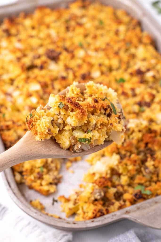 Spoonful of golden brown cornbread dressing lifted from the baking dish showing texture of sausage, veggies, and cornbread crumbs.
