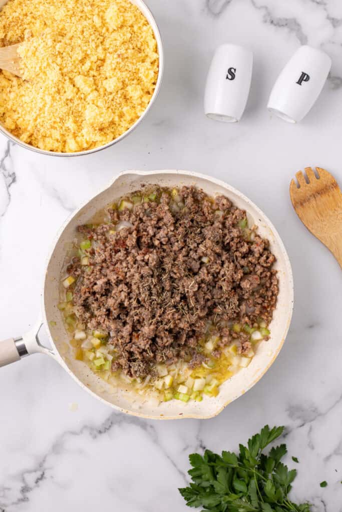 Skillet filled with cooked sausage, sautéed vegetables, broth, and seasonings ready to be mixed into cornbread dressing.
