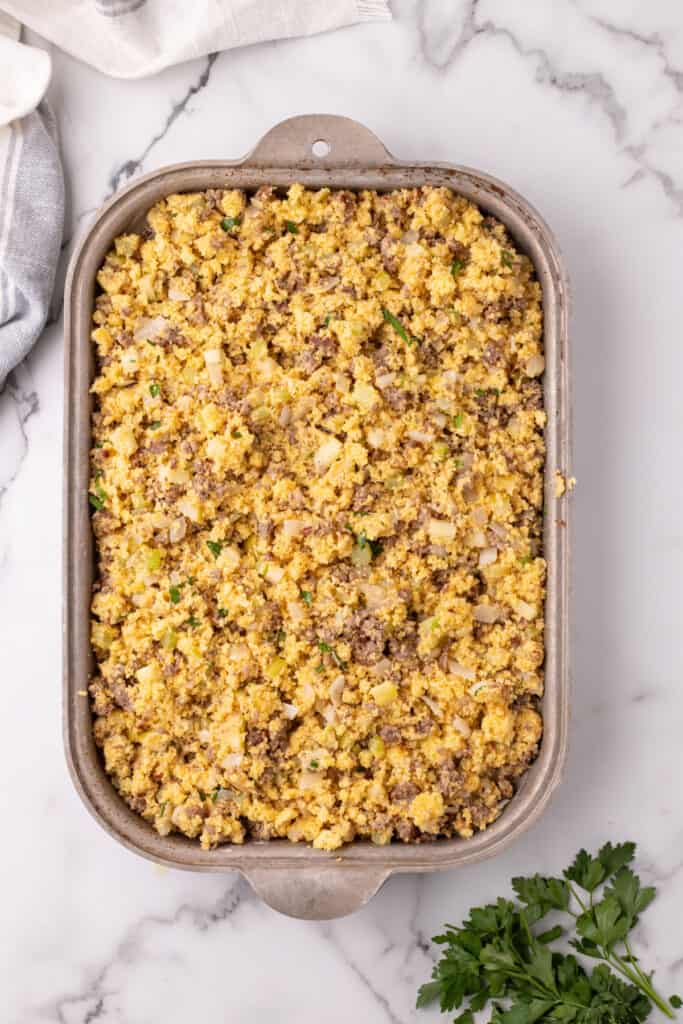 Baking dish filled with uncooked cornbread dressing mixture spread evenly and ready for the oven.