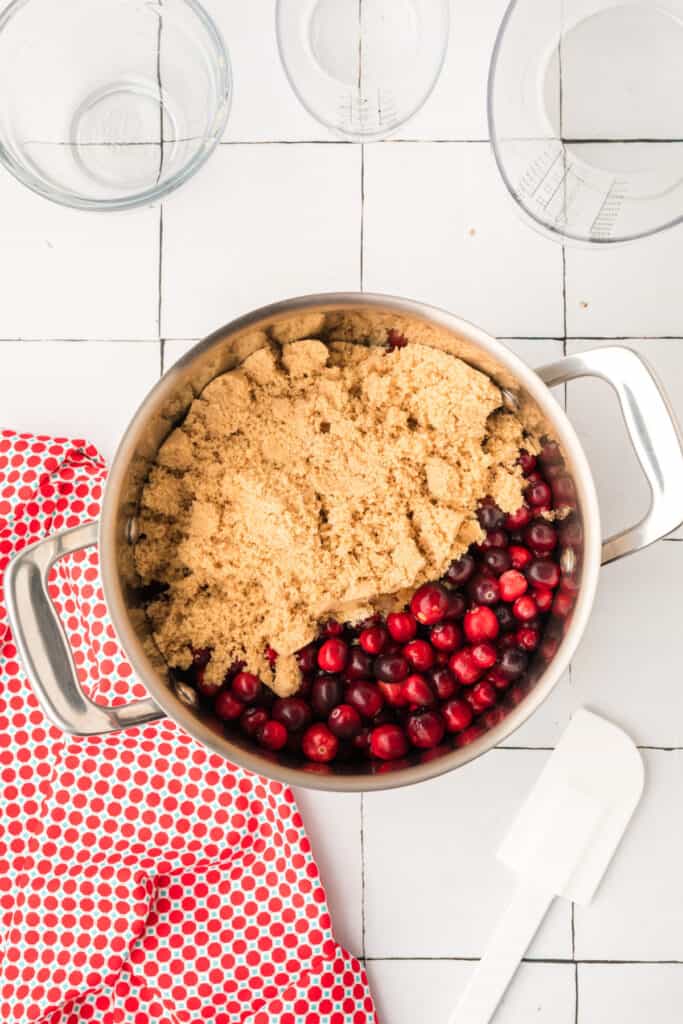 Large pot filled with fresh cranberries topped with packed brown sugar before cooking.