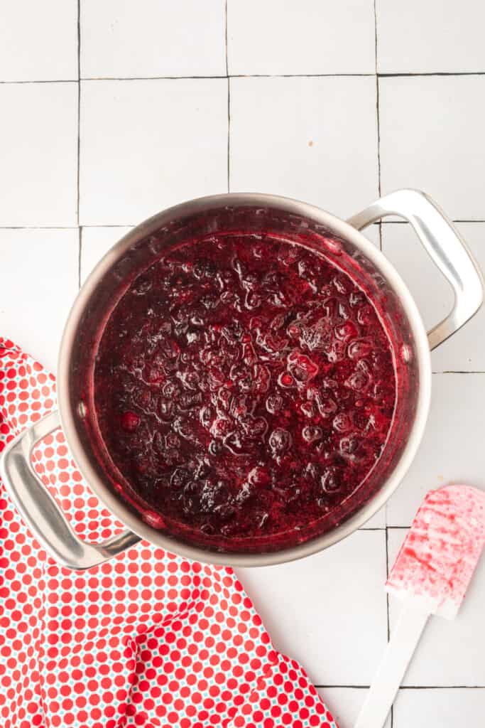 Cranberry mixture simmering in a pot as the berries burst and begin to thicken.