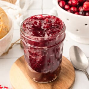 Close up of a full jar of cranberry jam showing chunky texture and deep red color.