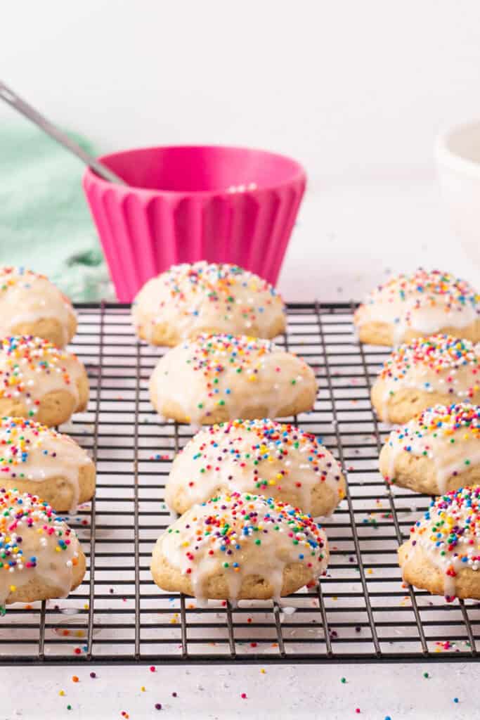 Glazed Italian Ricotta Cookies topped with rainbow sprinkles on a rack