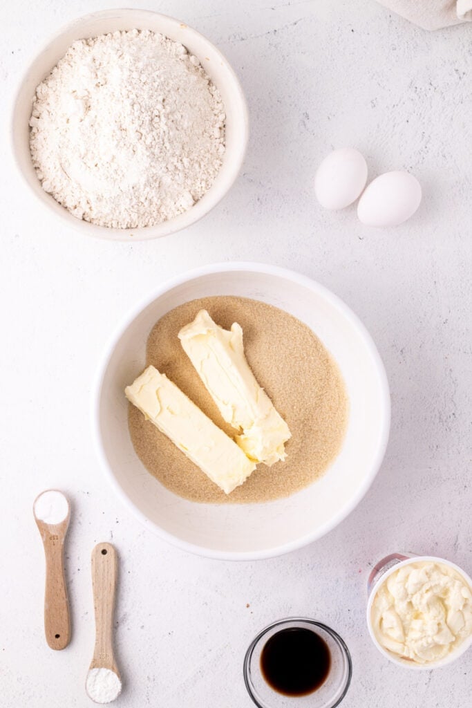 Butter and sugar in a white mixing bowl with other ingredients nearby