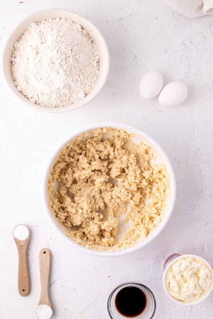 Creamed butter and sugar mixture in a bowl surrounded by remaining ingredients