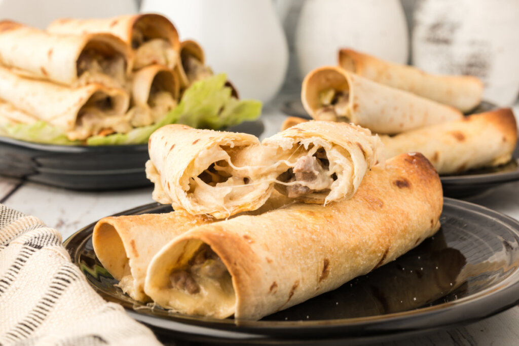 philly cheesesteak taquitos on black plate