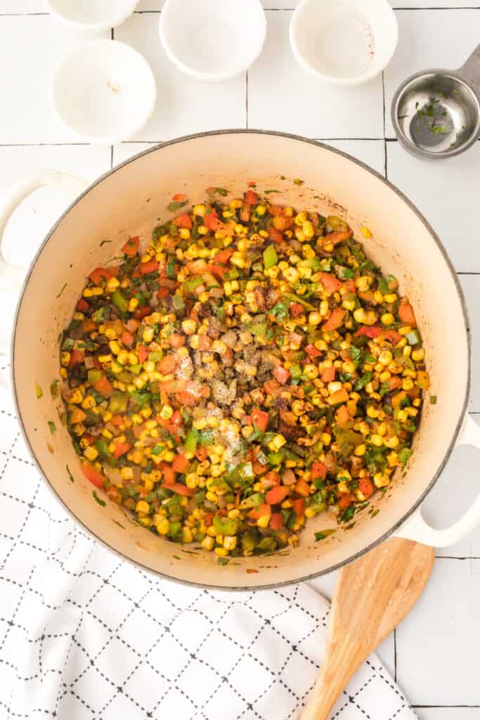 sautéed corn, diced peppers, and onions in a white pot with spices sprinkled on top