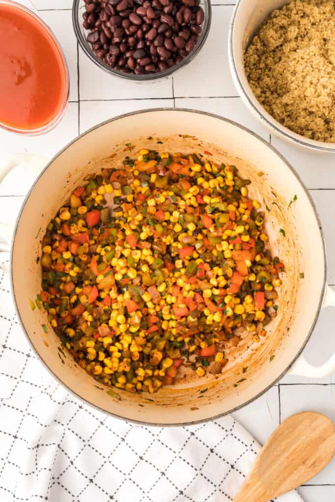 cooked corn and diced vegetables in a white pot with bowls of black beans and quinoa nearby