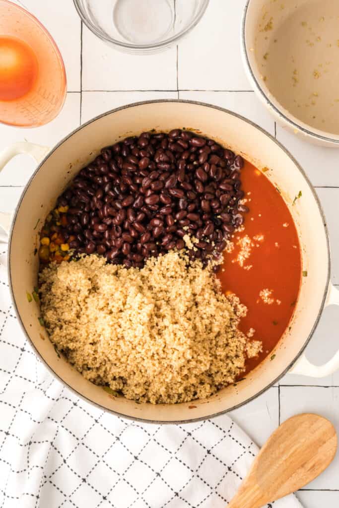 black beans, cooked quinoa, and enchilada sauce added to corn and vegetable mixture in a pot