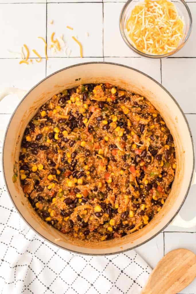 shredded cheese added on top of quinoa, black beans, and corn mixture in a pot