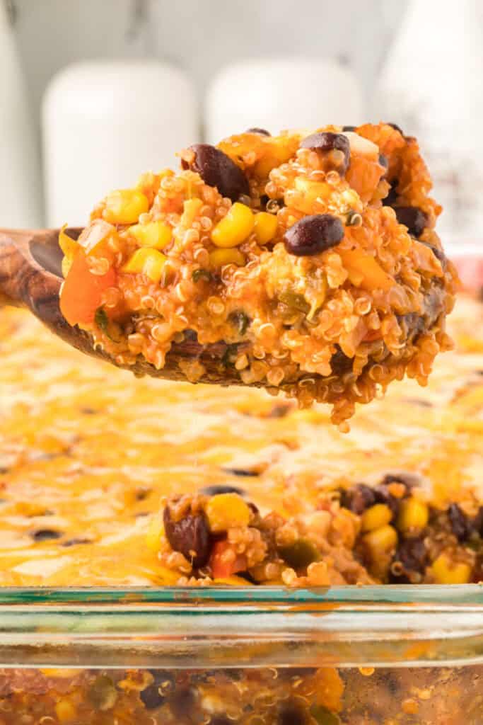 close-up of a wooden spoon lifting black bean corn enchilada quinoa casserole with melted cheese and visible quinoa, black beans, and corn