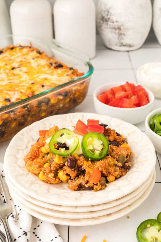 glass baking dish filled with black bean corn enchilada quinoa casserole next to a plated serving topped with jalapeno slices and diced tomatoes