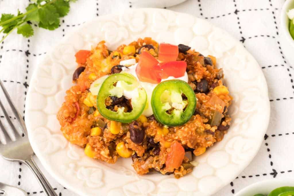 overhead view of a plated portion of black bean corn enchilada quinoa casserole with jalapeno slices, sour cream, and diced tomatoes