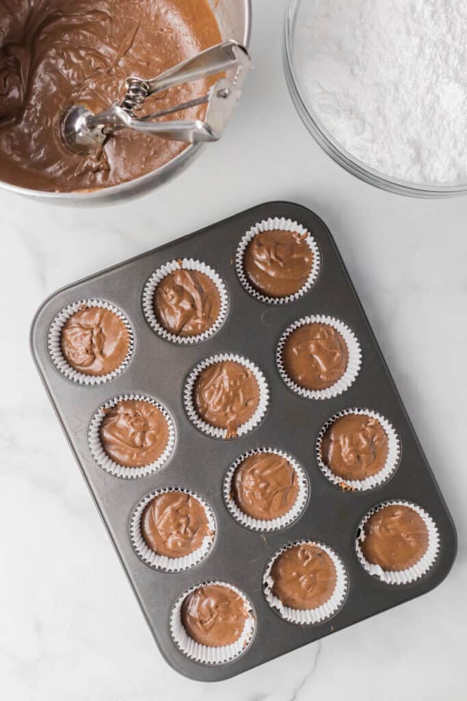 Chocolate cupcake batter portioned into paper-lined muffin cups before baking
