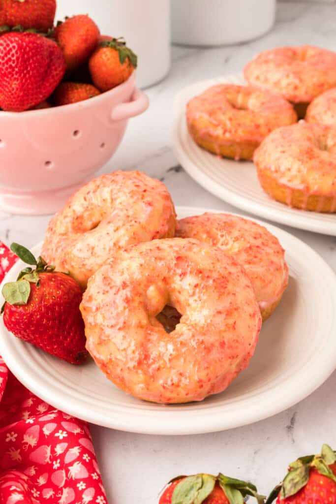 three vanilla cake donuts with strawberry glaze on a plate