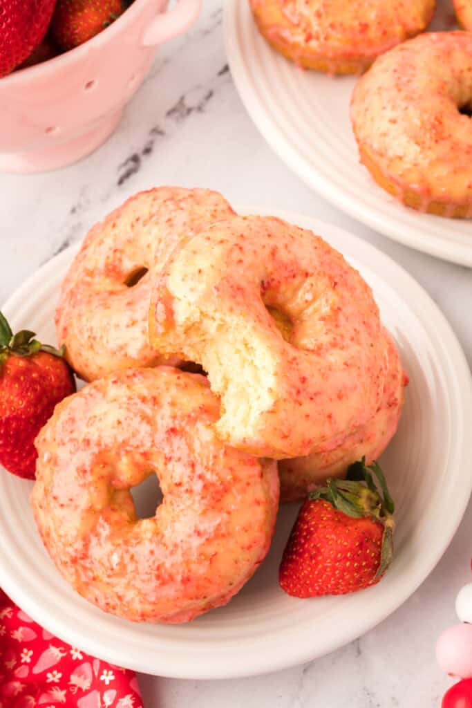 three vanilla cake donuts on plate one with a bite